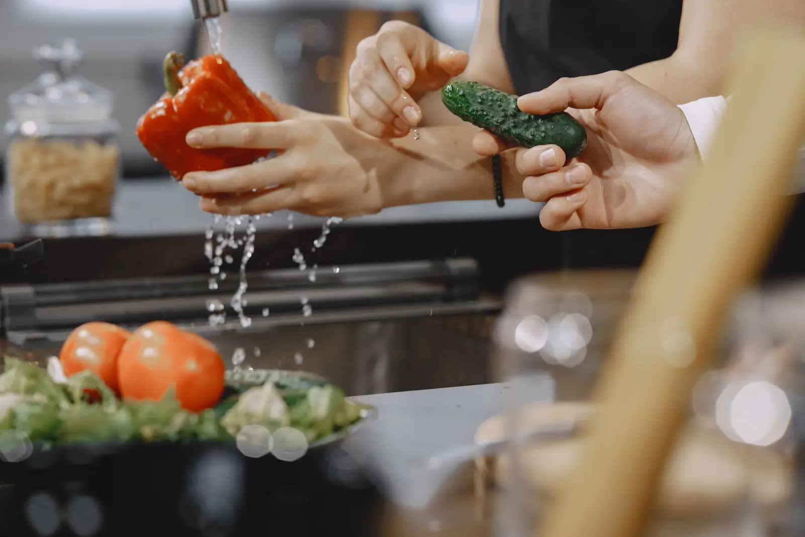 Hands rinsing vegetables under running water at a kitchen sink