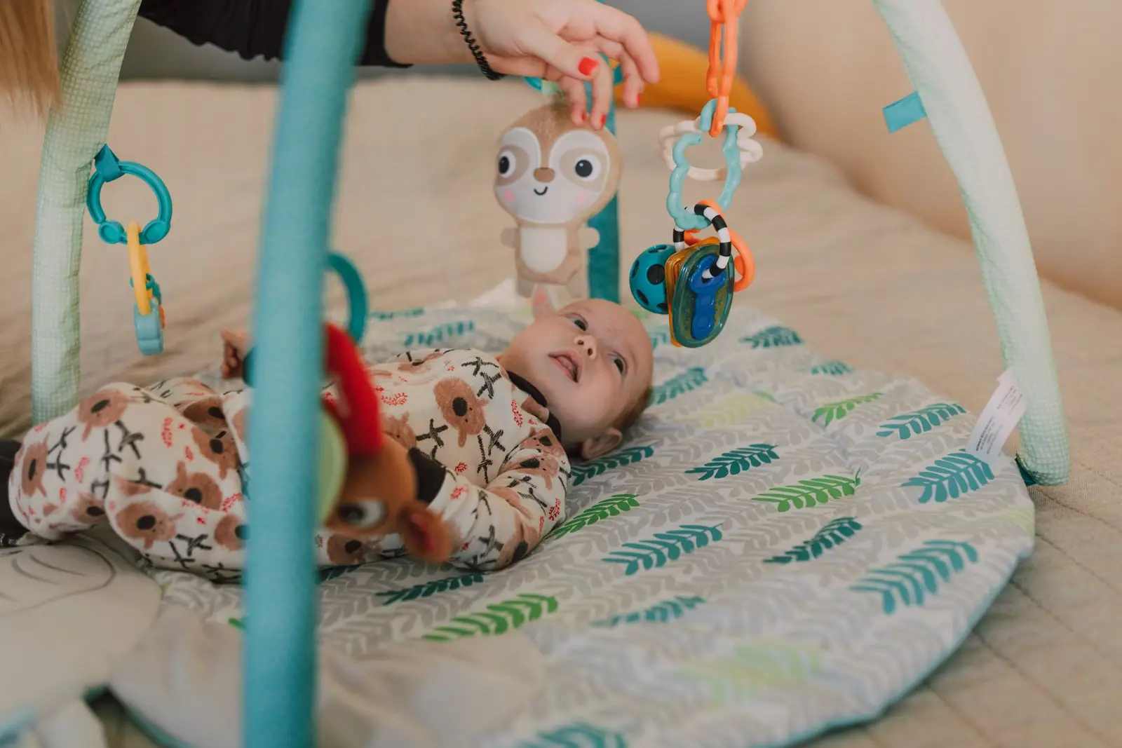 An adult holding owl-shaped hanging toys above a baby on a quilted play mat