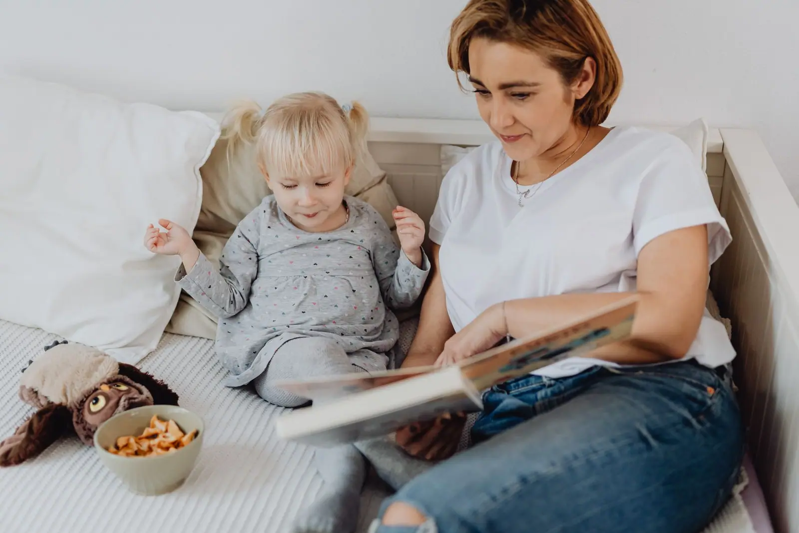 An adult reading a book beside a young child on a sofa