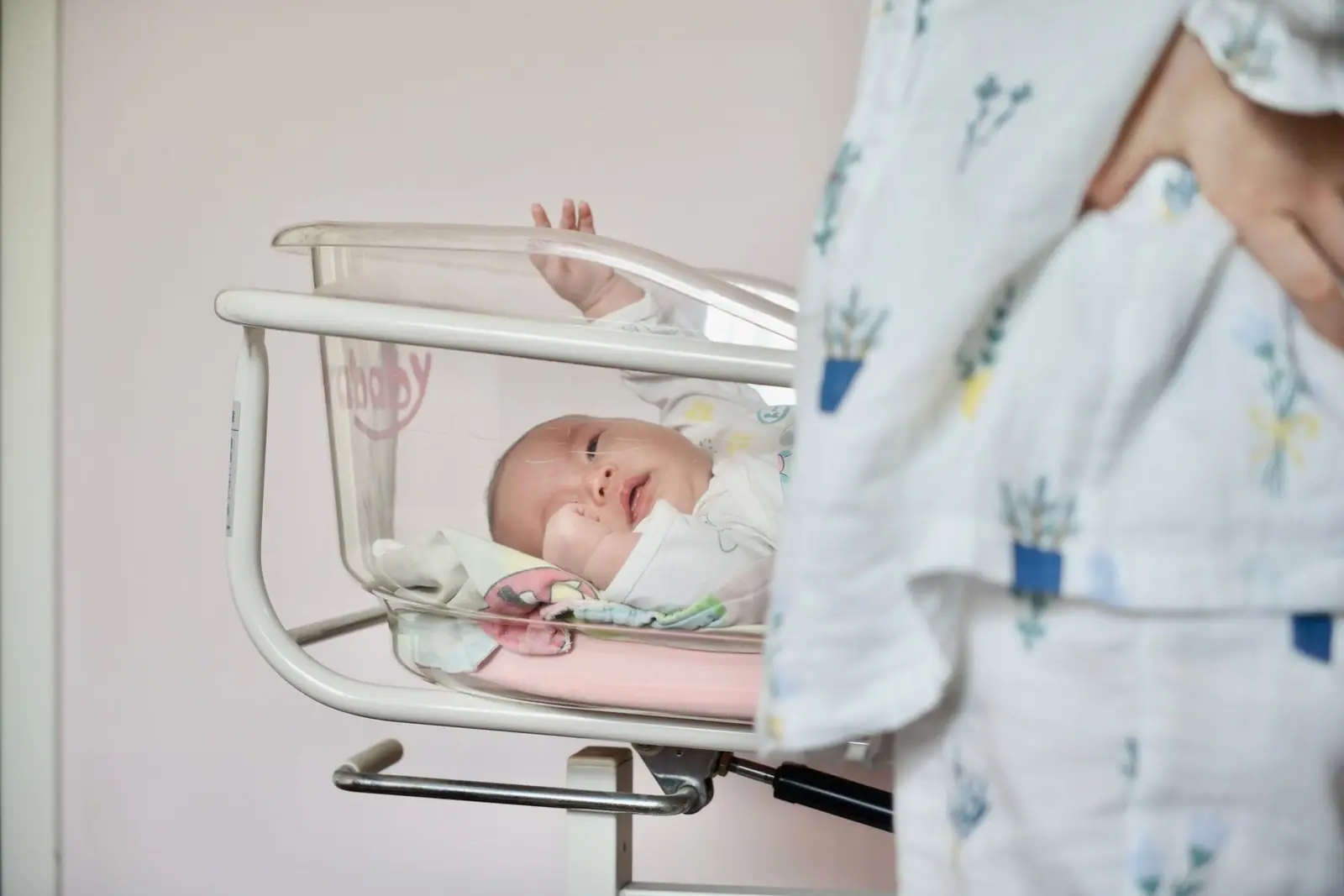 A newborn lying flat in a clear hospital bassinet