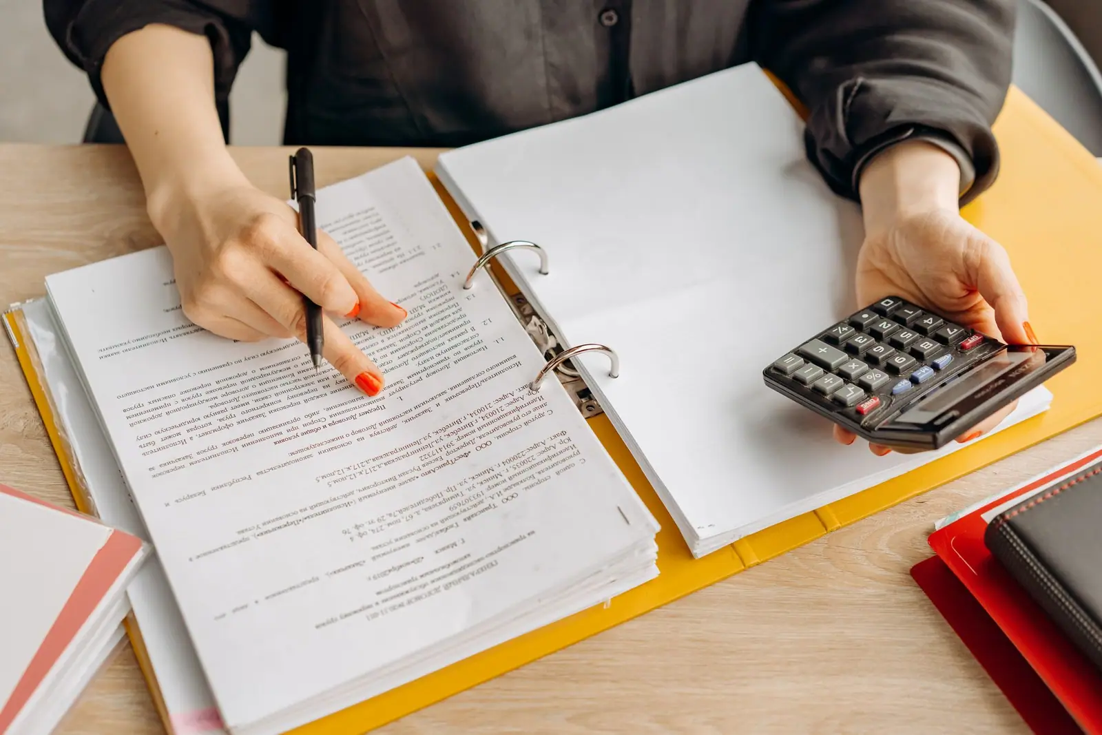 A person working through printed documents with a pen and a calculator