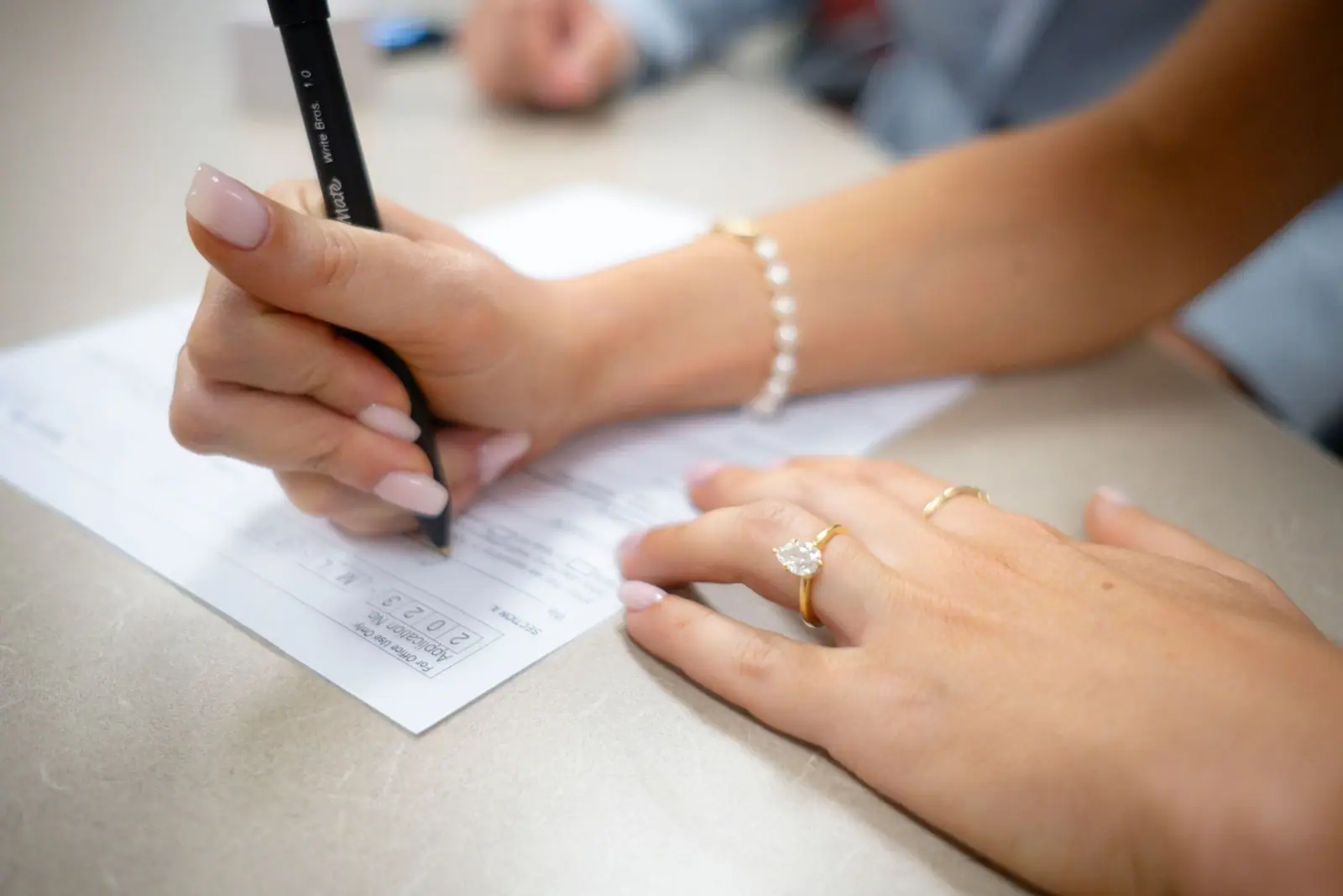 Hands writing with a black pen on a paper form at a table