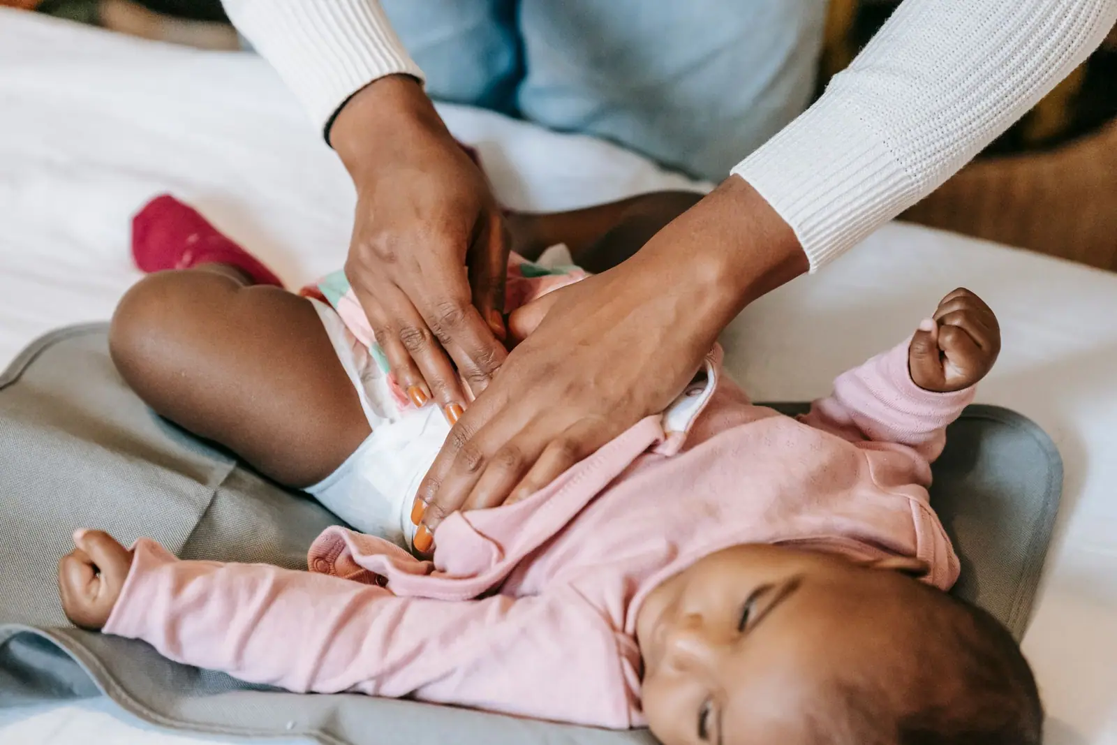 An adult fastening a diaper on a baby lying on a padded changing surface