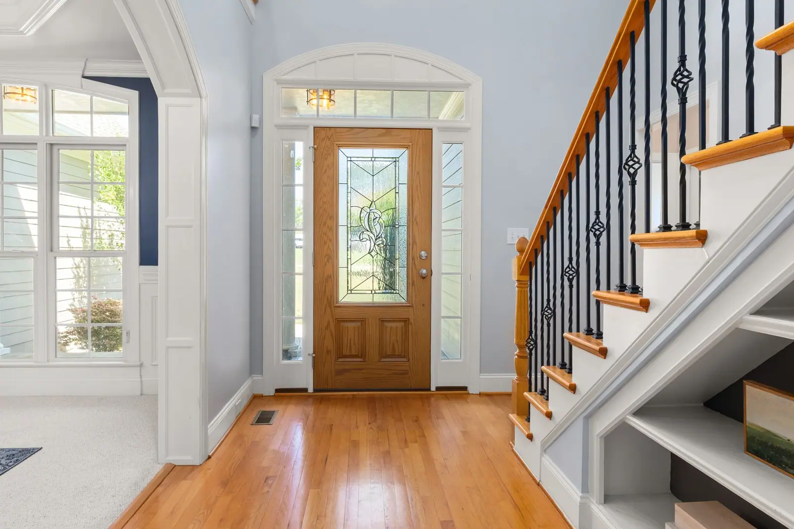 An interior staircase with wooden handrail and dark balusters beside a front door