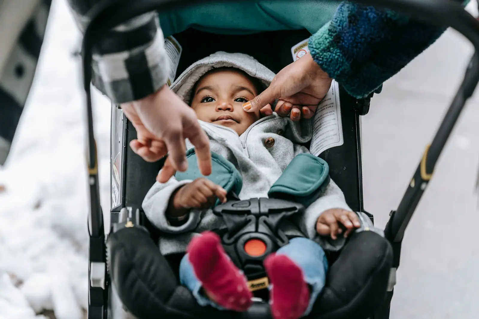 An adult fastening a baby into a stroller seat