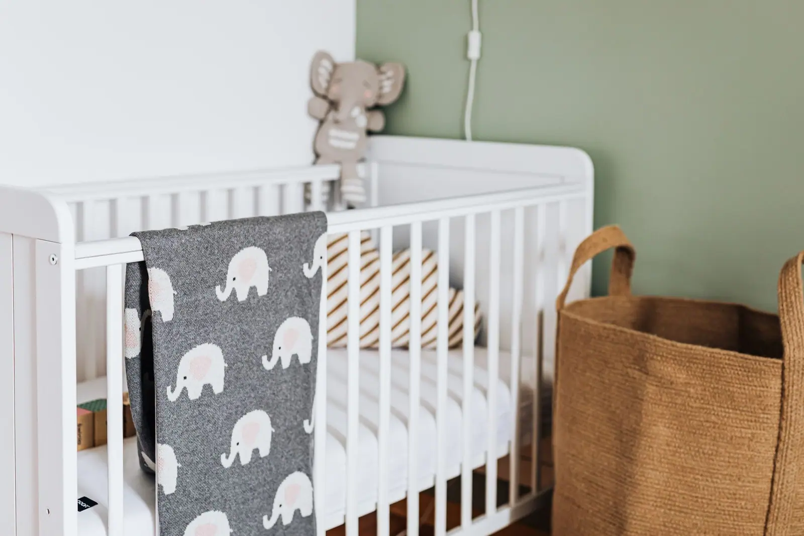 A white crib in a staged nursery with an elephant-pattern blanket draped over the rail