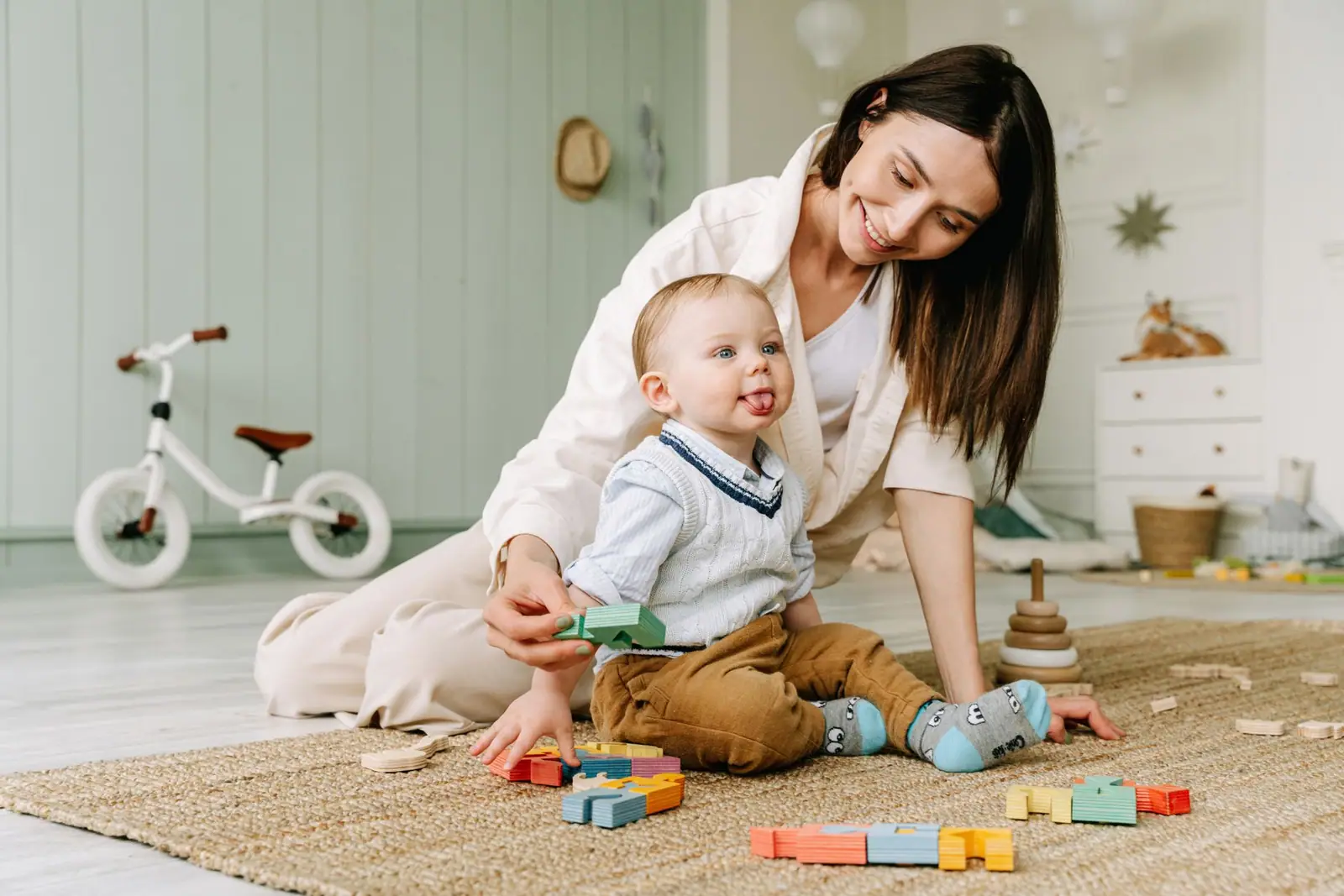 An adult sitting on the floor beside a young child playing with colorful blocks