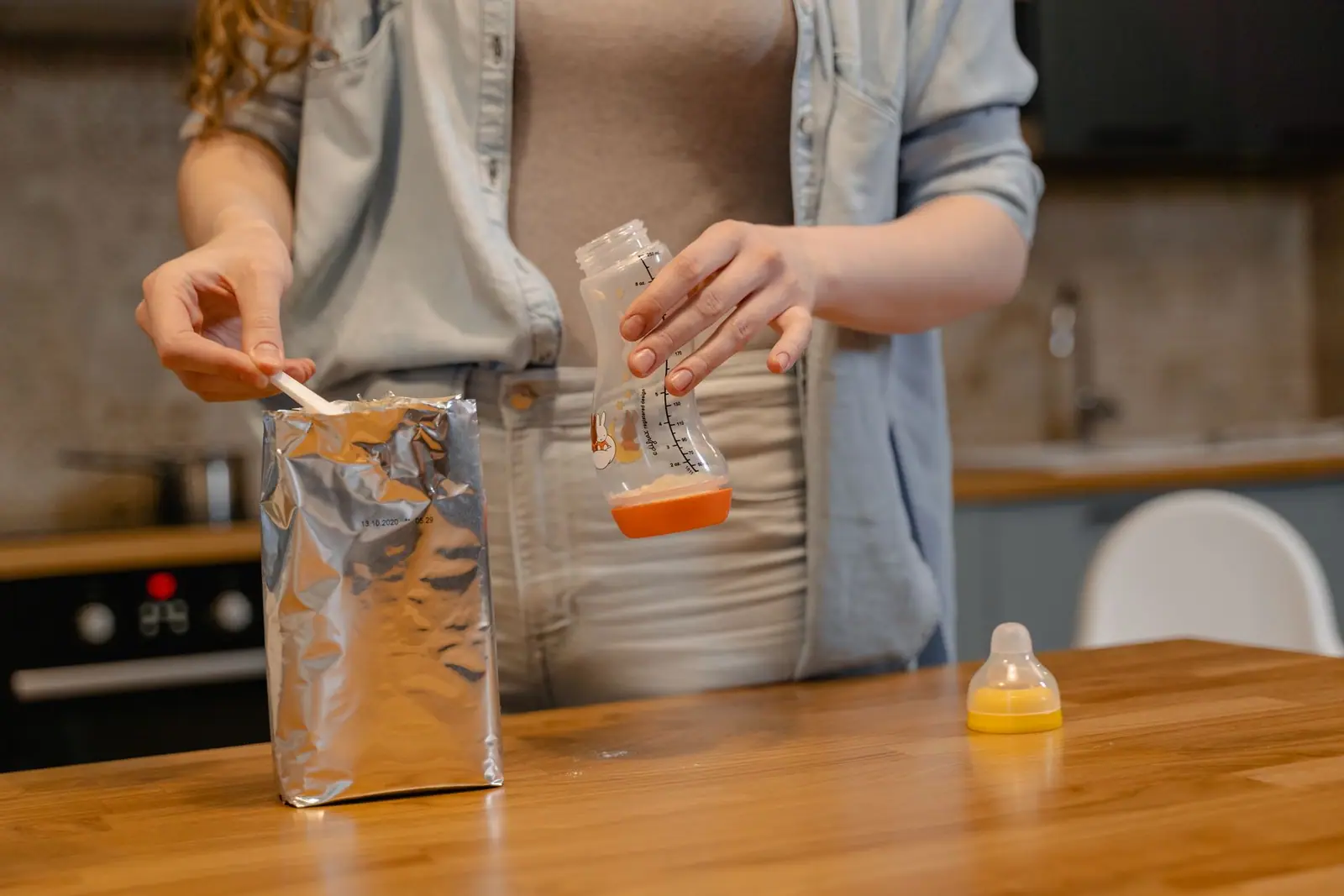 An adult measuring powdered formula over a feeding bottle