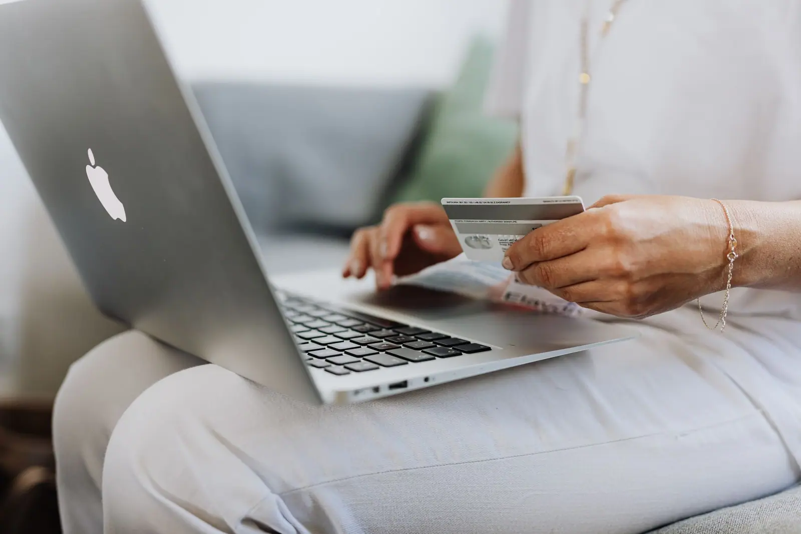 A person holding a payment card while using a laptop on a sofa